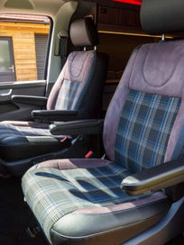 View into the front cabin of a van showing matching grey tartan upholstered driver and passenger seats