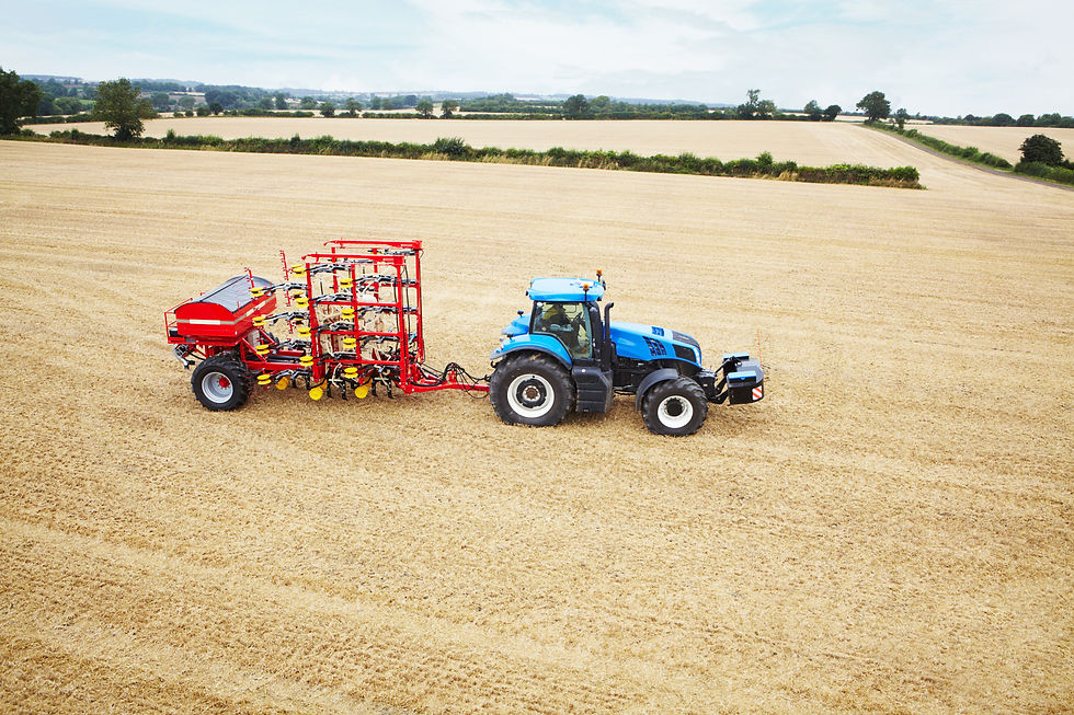 High-angle shot of a blue tractor towing a large red seeder across a harvested field.