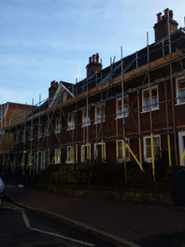Rows of terraced brick houses with roof level scaffolding erected along the street side