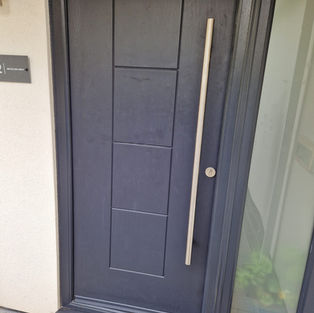 Sleek modern front door in dark gray with vertical handle, rectangular panels