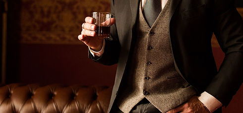 Groom holds in his hand a glass of whiskey indoors