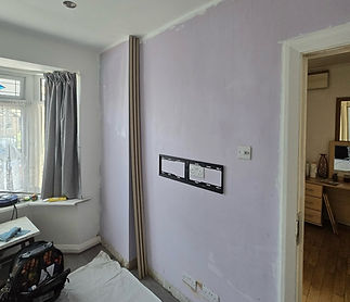 Room setup for mounting a TV on a light purple wall with a bracket above electrical outlets