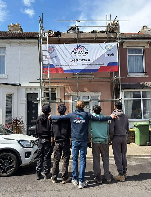Five roofers standing together looking up at scaffolding and a company banner on a terraced house front