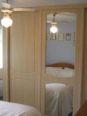 Bedroom with light wood wardrobes featuring mirrors, a ceiling fan, soft lighting