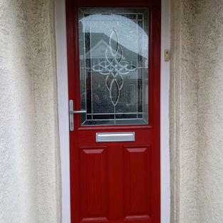 A vibrant red door with decorative glass design, framed by light stucco walls,