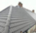 Steep roof with neat, dark gray, interlocking tiles and two brick chimneys