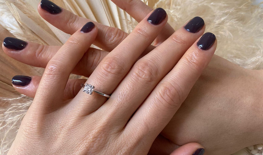 Close up of a hand showcasing a fresh dark purple gel manicure with a gold ring