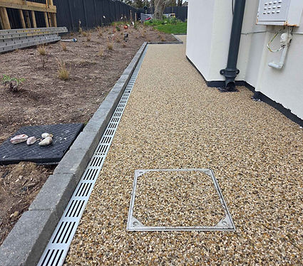 Gravel pathway beside a white building with a drainage grate along the edge