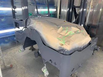 Forklift chassis undergoing preparation and masking in a spray booth, with parts covered with brown paper before painting