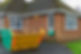 A medium-sized yellow and green skip sitting on the driveway of a brick house
