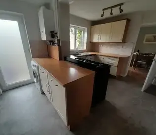 Kitchen with wooden countertops, light-coloured cabinets, and a dark stove