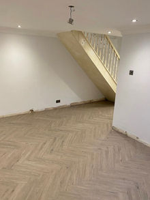 Empty interior room featuring newly laid light oak herringbone parquet flooring and wooden stairs