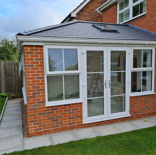 A small, red-brick house extension with white-framed windows and patio door