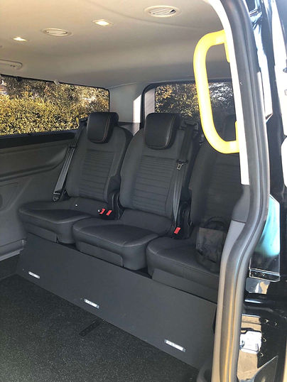 The interior of a minibus showing three black passenger seats with seatbelts