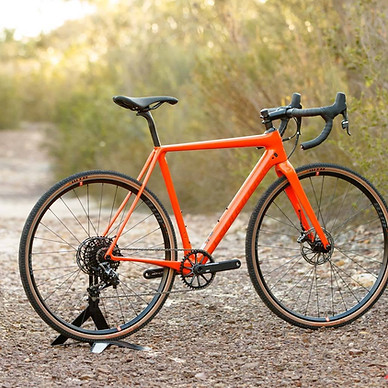 Bright orange gravel bike with tan sidewall tyres parked on a gravel trail