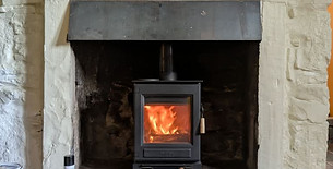 A black log burner with a burning fire inside a rustic stone fireplace