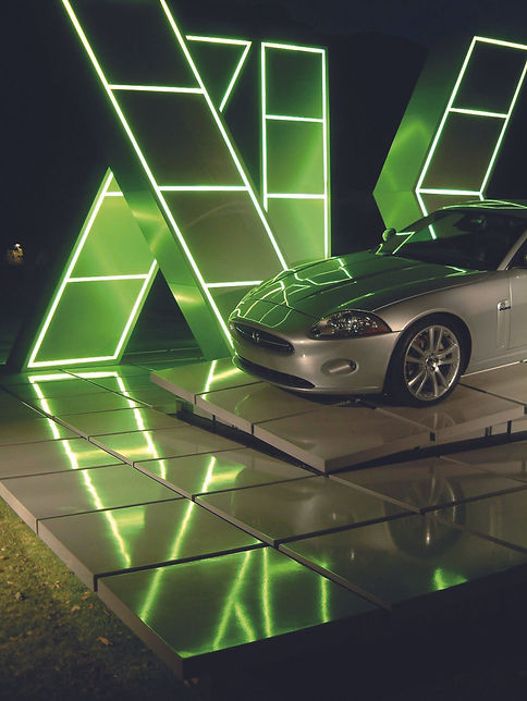 Silver Jaguar car displayed on a tiled platform before large green illuminated geometric structures