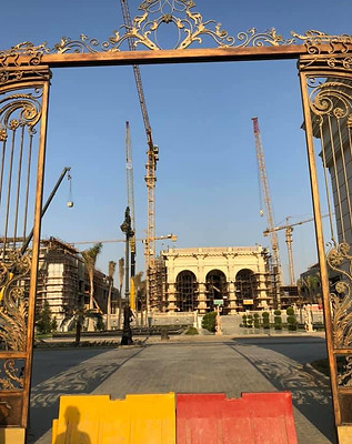 Ornate golden gate frames a construction site with cranes and a scaffolded building