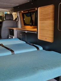Extended blue rock and roll bed positioned next to black and oak camper conversion cabinets