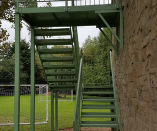 The image shows an outdoor green-painted structural steel staircase and elevated platform system