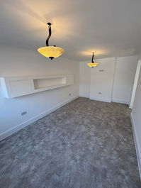 Spacious empty living area featuring textured grey carpet and two ceiling light pendants