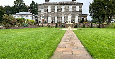 Stone path leading through a lush green lawn to a large manor house.