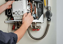 A person adjusts a panel on an open gas boiler, revealing pipes