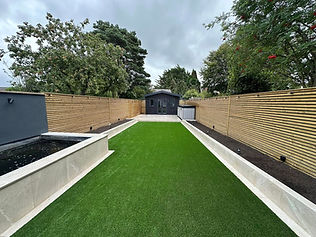 Finished garden featuring artificial grass lawn and grey stone paving slabs