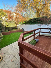 Outdoor garden featuring a wooden deck, artificial grass, and autumn trees
