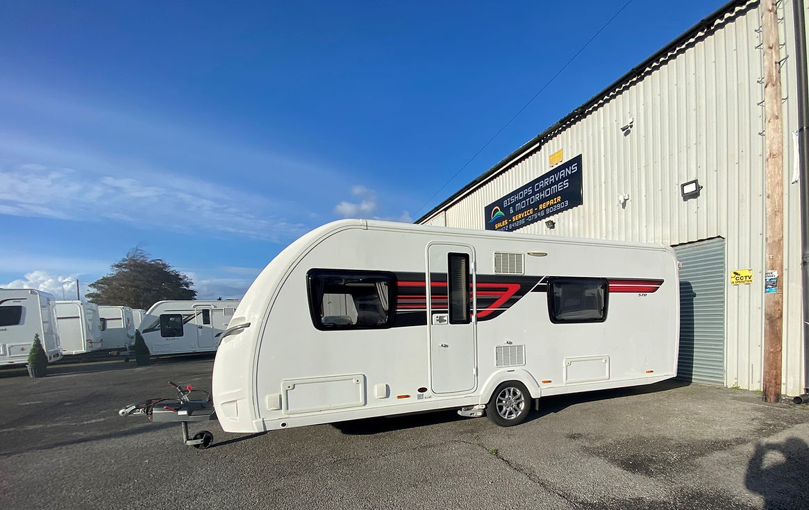 A white caravan with red and black stripes is parked outside