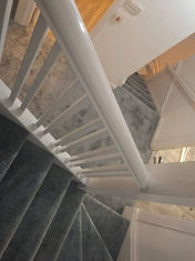 Top-down view of a winding staircase with grey carpet and white wooden banisters