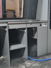 Custom grey storage units and shelving being fitted into a van during the camper conversion process