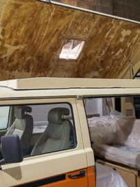 Classic orange and cream VW camper van with its pop top roof shell lifted in a workshop