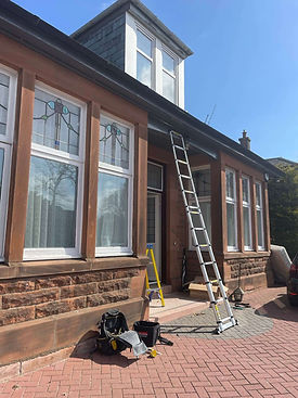 Brick house with tall stained-glass windows in sunlight, undergoing maintenance