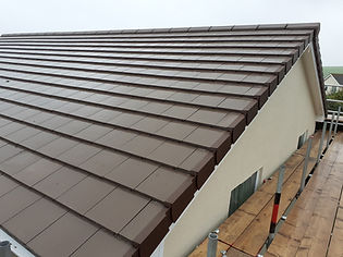 A neatly tiled, brown gabled roof on a beige building viewed at an angle