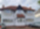 A quaint two-story white house with a red-tiled gable roof and a small front porch