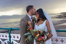 Bride in a white dress and groom in a suit share an intimate moment on a pier