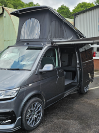Grey Volkswagen camper van parked outside with its pop top roof