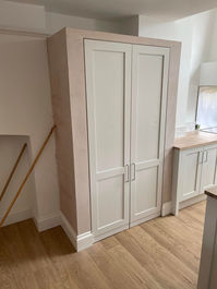 Built in white wardrobe storage cupboards fitted against a painted wall in a home interior