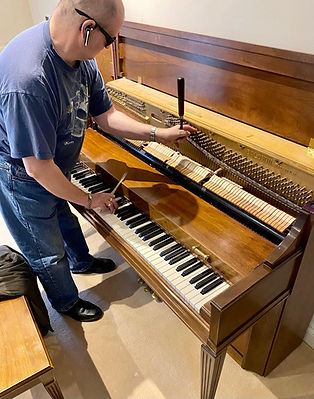 A person tunes an upright piano, using tools on the open strings