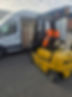 A worker in an orange safety vest operates a yellow forklift