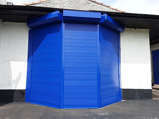 A bright blue, angular metal shutter covers the corner of a white and black building