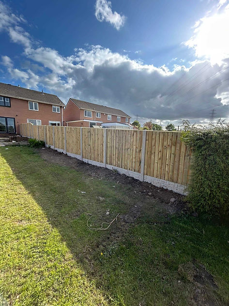 A wooden fence lines a grassy yard under a partly cloudy sky