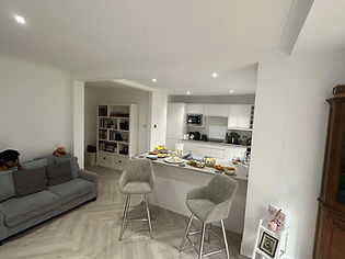 Open plan living area with grey sofa, kitchen island, bar stools, and herringbone floor
