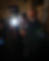 A bald man holding a camera with a microphone attached is filming in a dimly lit room