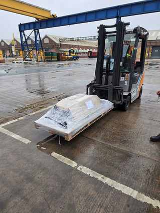 A forklift transports a pallet wrapped in plastic across a wet industrial yard