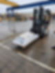 A forklift transports a pallet wrapped in plastic across a wet industrial yard