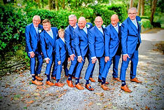 Groomsmen and a young boy in matching blue suits and brown shoes pose playfully