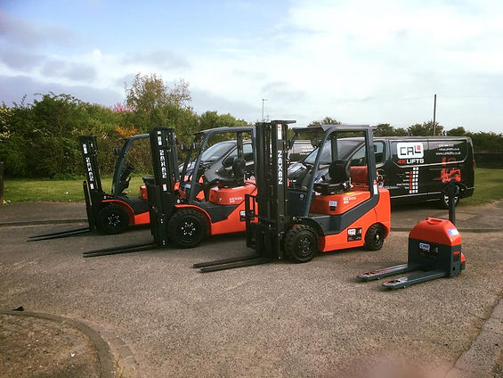 Three red and black Nexen forklifts are parked outdoors near black vans