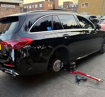 Black car with a rear wheel removed, raised by a jack